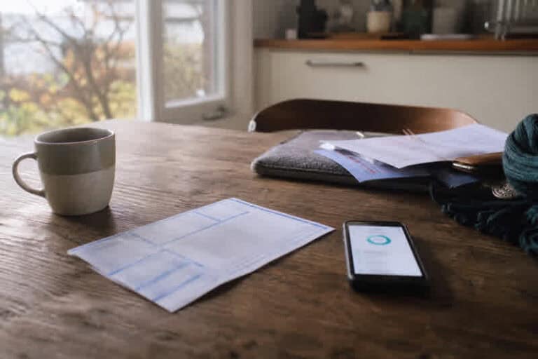 Paperwork, a smartphone and a cup of coffee on a wooden table by a window.