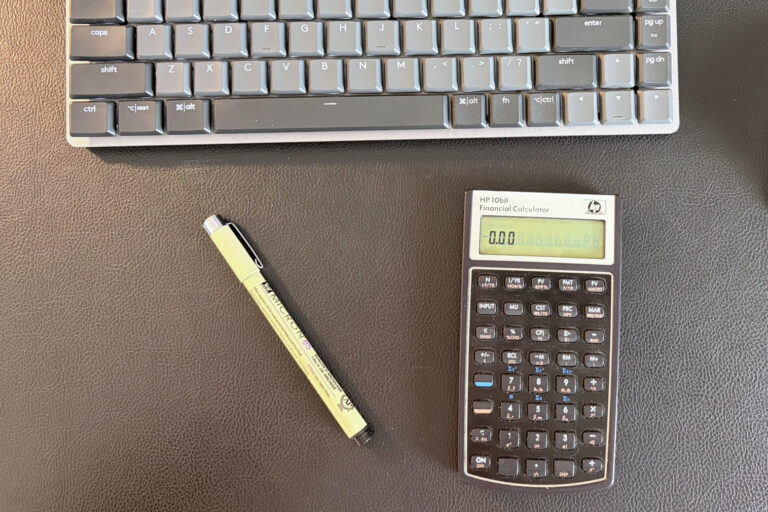 A financial calculator and pen on Daniel Nel's desk, with part of a keyboard above.
